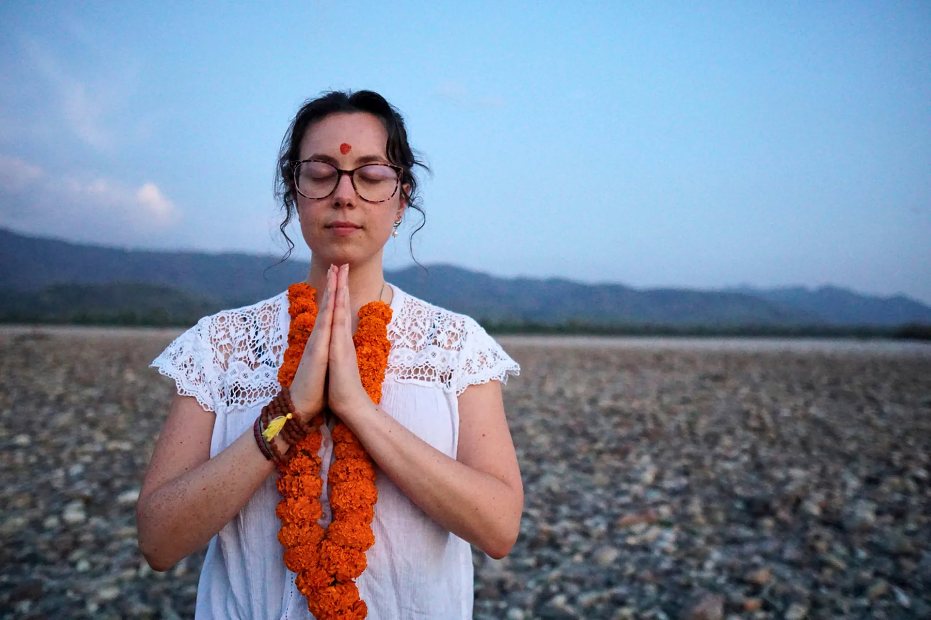 Student in a namaste meditation pose by the Ganga during a 7-day retreat in Rishikesh