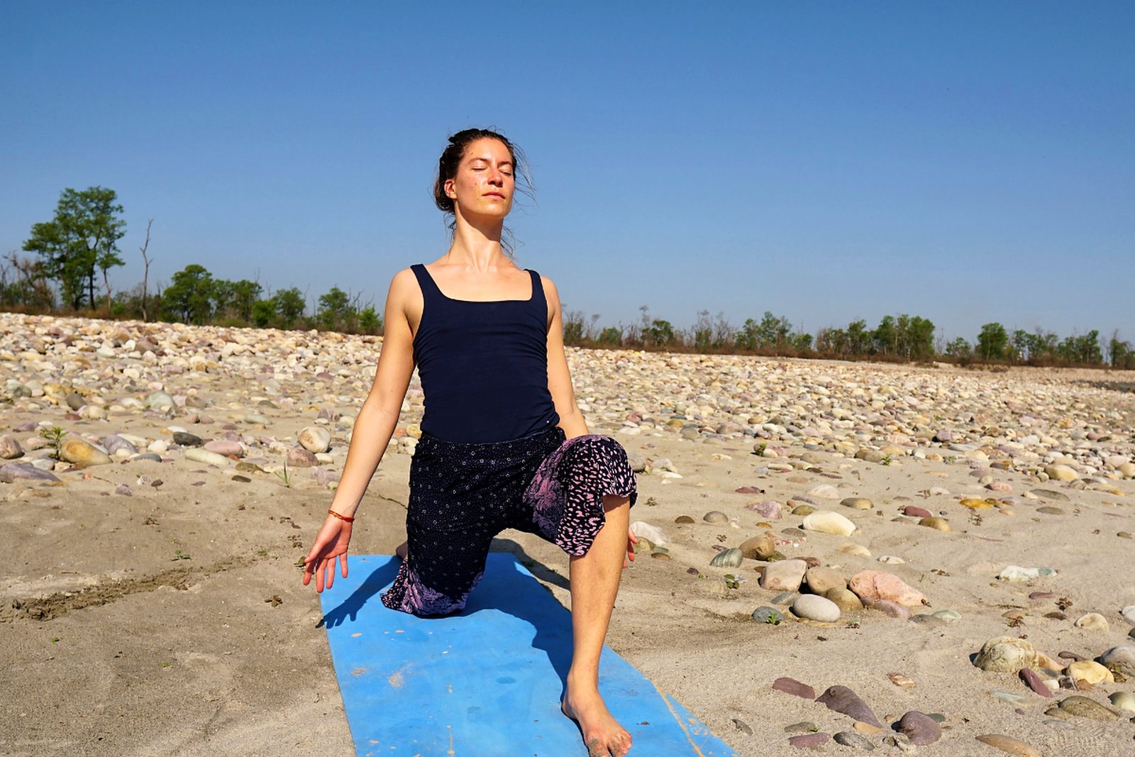 Crescent lunge yoga pose on the riverbank in Rishikesh