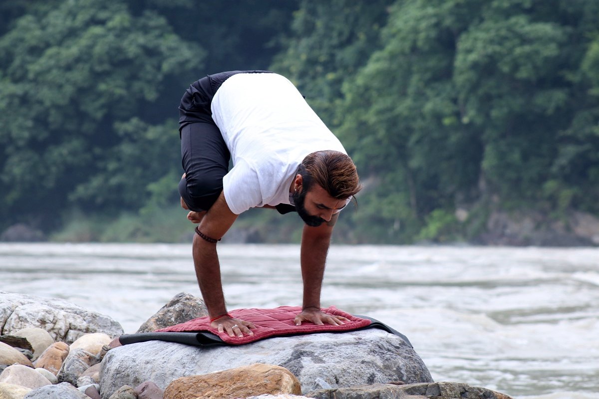 Student practicing crow pose by the Ganga in Rishikesh