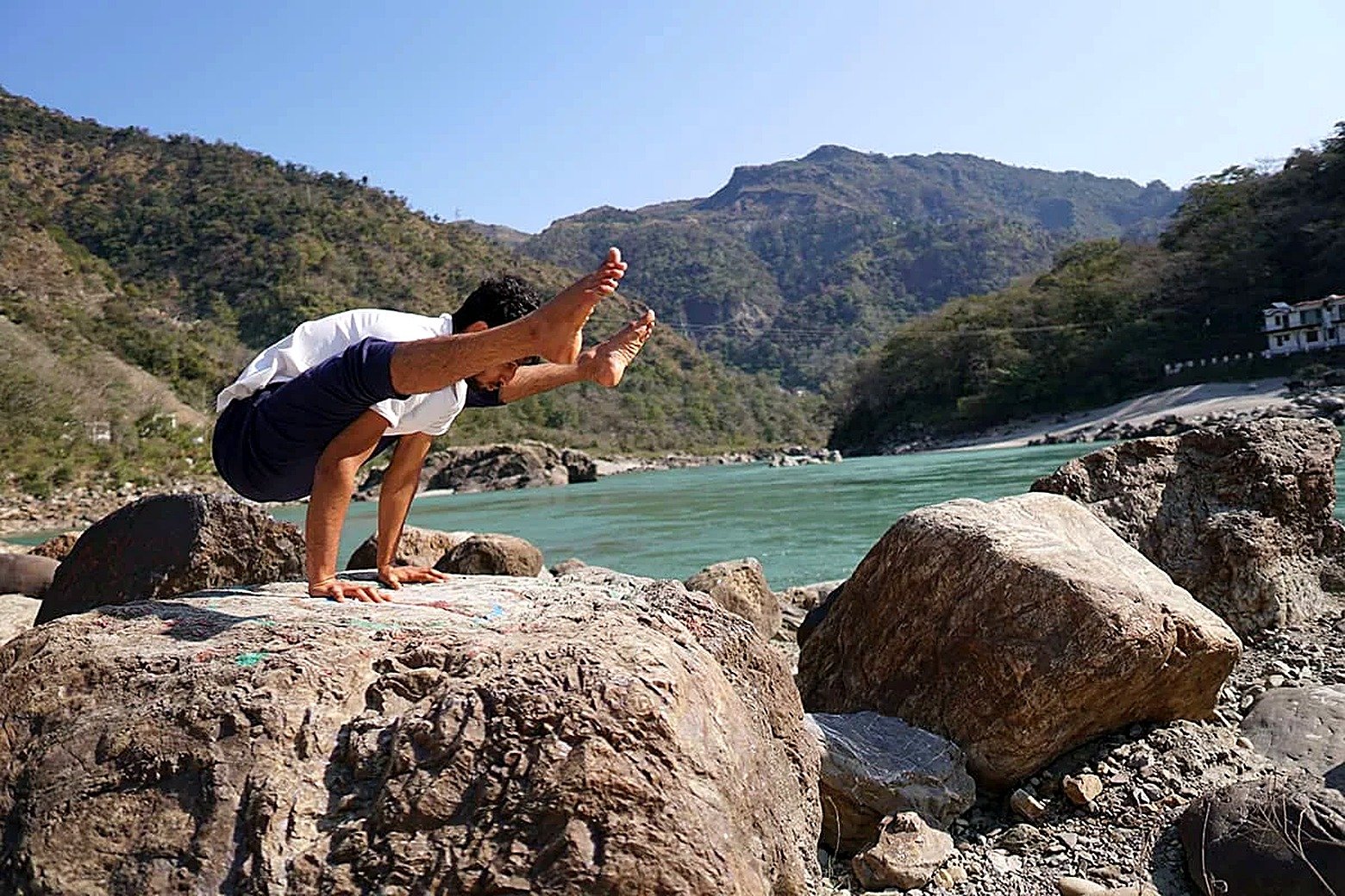 Crow pose practice on a riverside rock during the detox retreat