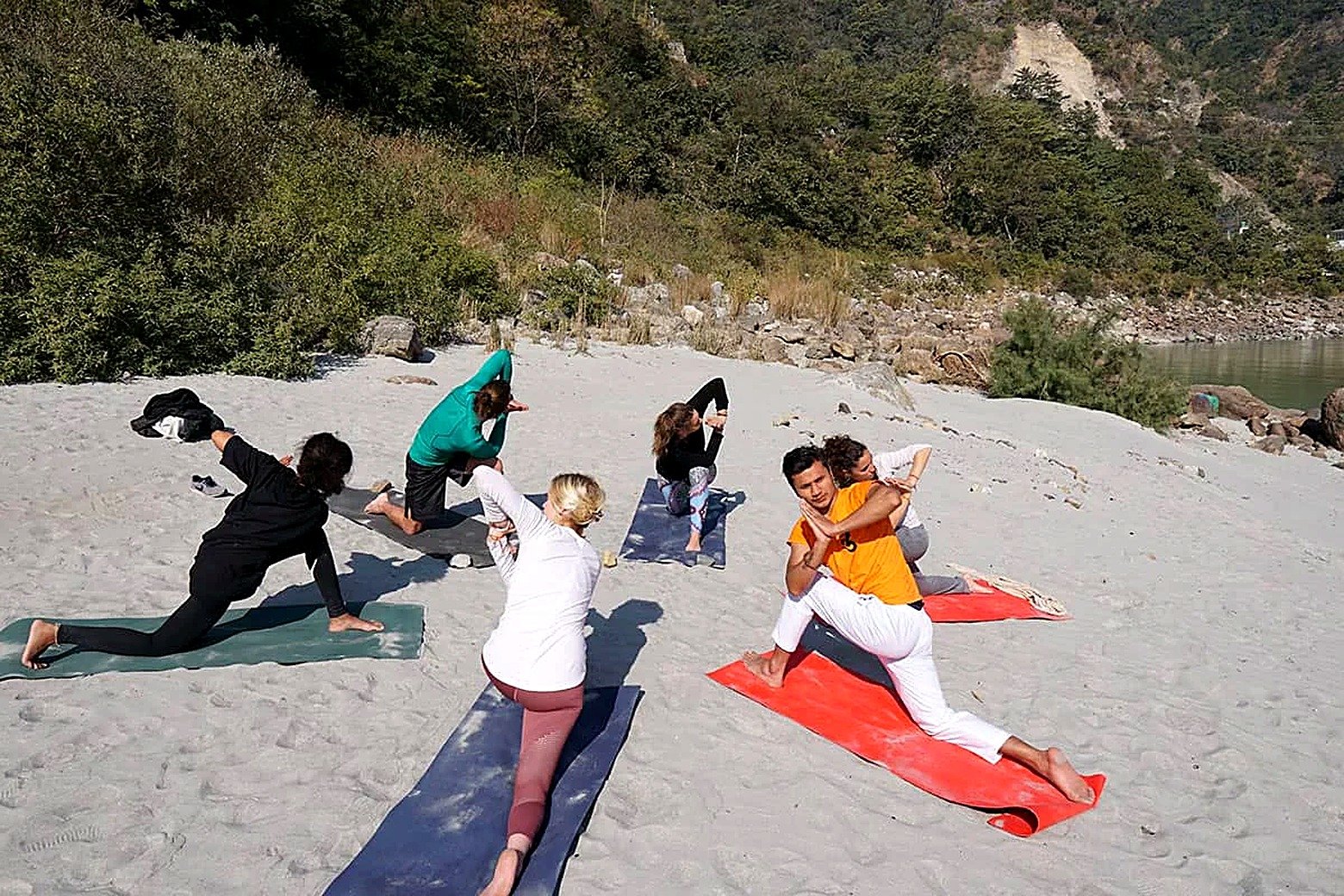 Beginners practicing yoga together on a sandy Ganges riverbank in Rishikesh